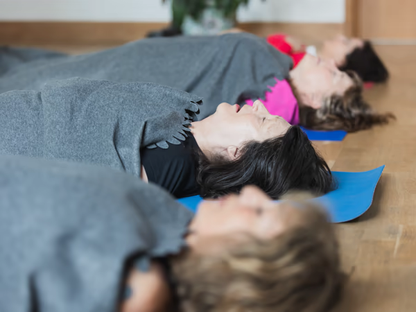 Women resting under blankets on yoga mats during a breathwork session with Giselle Monbiot